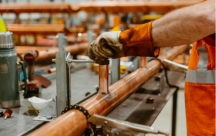 Worker welding copper pipe in Sauer Group manufacturing facility.