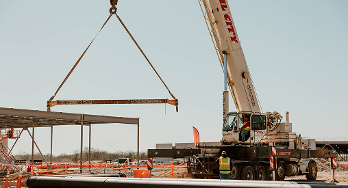Construction crane lifting a steel beam at a building site.