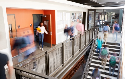 Busy school corridor with stairs and people walking by.